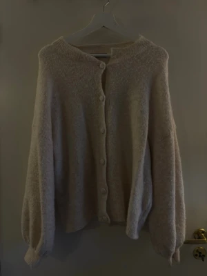 Beige fluffig kofta med knappar - Mysig beige kofta med fluffig textur och stora knappar framtill. Koftan har ballongärmar och ribbade muddar vid ärmslut och hals. Perfekt för lager på lager och en avslappnad look.Hör av dig om du har några frågor! 💗🫶🏼