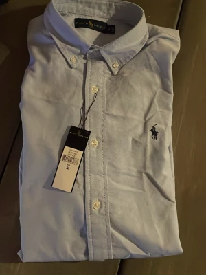 Ralph lauren skjorta - En Ralph lauren skjorta i ljusblå, är typ helt ny bara använts vid enstaka tillfälle. Sitter som vanlig M och passar till det mesta. Hör av er vid fler frågor eller så köper man direkt så fraktar jag!