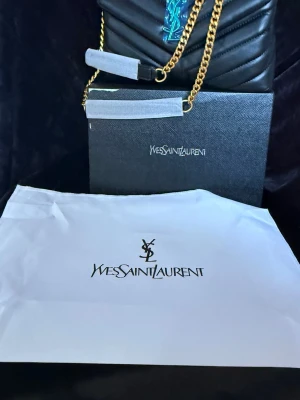 Svart  handväska med guldkedja - Snygg svart handväska med quiltat mönster, guldfärgad kedjerem .Och har dragkedja samt medföljande dustbag och originalkartong.