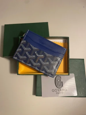 Blå Go4yard korthållare i läder - Säljer en snygg blå korthållare från Go4yard med det klassiska vita och gråa Go4yard-mönstret. Tillverkad i exklusivt läder och har flera fack för kort. Kommer med originalask och dustbag. Perfekt för dig som vill ha något stilrent och lyxigt i fickan.