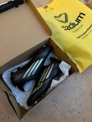 Adidas F50 Storlek 43.5  - Helt nya och aldrig använda. Levereras i originalförpackning med kartong. Köptes till min son, men han bestämde sig för att sluta spela fotboll, så de har aldrig använts. Lätta fotbollsskor designade för snabbhet och prestation på planen.  Jag har även matchande benskydd och strumpor tillgängliga på min profil. Tveka inte att skicka ett meddelande om du har några frågor.