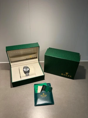 silverfärgad klocka i stål - Snygg och klassisk klocka i silverfärgat stål med länkarmband och rund urtavla. Kommer i original grön med certifikat och tillbehör. Perfekt för dig som vill ha en tidlös accessoar med exklusiv känsla.