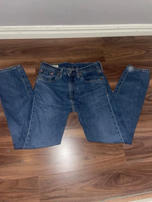 Levi's blå raka jeans W 28, L 30 - Klassiska blå jeans från Levi's med rak passform och fem fickor. Jeansen har en tidlös tvätt, knappgylf och detaljer som den röda Levi's-lappen bak. Perfekta till vardags för en avslappnad look. Tillverkade i slitstark denim. Knappt använda kanske ett fåtal gånger ca 4-5 gånger pris går att diskuteras vid en snabb och enkel affär!👍🏼.                     Säg gärna till om ni vill ha fler bilder eller om ni har några frågor!