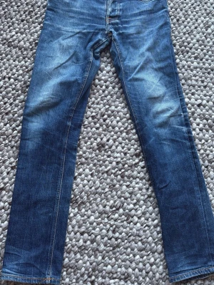 Nudie Jeans Grim Tim Dry Open Navy- W31 L34 - Nudie Jeans Grim Tim Dry Open Navy - W31 L34.  Bra skick. Fina naturlig patina. Skrev lagat hos Nudie Jeans i Göteborg. Båda framfickorna lagade samt pyttelitet hål lagat på insidan vänsterbenet mot sömmen hos Nudie Jeans i Stockholm.  98% bomull 2% stretch  Kontakta mig gärna för frågor och för prisförslag. Midja 39 cm Längd 104 cm Innerbenslängd 80 cm