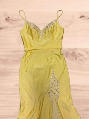 Balklänning gul - Säljer min balklänning från 9ans bal. Lång, fin gul klänning med slit och detaljer med stenar. Köpt i en bal/bröllopsbutik. Använd en gång och kemtvättad efter.