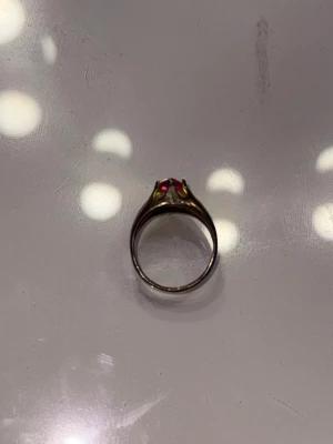 Guldfärgad ring med rosa sten - Cool ring i guldfärgad metall med en stor, rund rosa sten i mitten. Ringen har en klassisk form och stenen sitter i en upphöjd fattning som verkligen drar blickarna till sig.