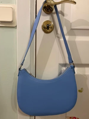 Ljusblå axelväska  - Trendig ljusblå handväska med axelrem. Materialet är slätt i någonslags skinnimitation. Den är från Gina tricot💕