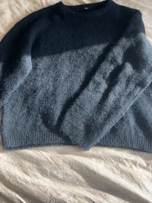 Mörkblå stickad tröja från 157 - Mysig mörkblå stickad tröja från 157 med rund halsringning och långa ärmar. Tröjan har en fluffig, mjuk struktur och ribbstickade muddar vid ärmslut och nederkant. Perfekt för kyliga dagar och enkel att matcha med jeans eller kjol.