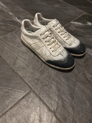 Vita och mörkblå sneakers från Maison Margiela - Säljer ett par Maison Margiela sneakers i vitt och mörkblått de är i rätt fint skick men lite slitet inuti vid hällen. Vid snabb kan man såklart pruta!! Skriv vid minsta lilla fundering? Tar gärna byten!!!