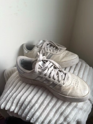 Beige Adidas sneakers i mocka - Säljer ett par beige Adidas sneakers i mocka med klassiska tre ränder på sidan. Skorna har lågt skaft, perforerade detaljer på tån och matchande beige snörning. Perfekta för dig som gillar stilrena och tidlösa sneakers.