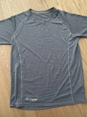 Grå tränings-tshirt  - Snygg grå tränings-tshirt från 157 Funk med korta ärmar och rund hals. Det är i ett snabbtorkande funktionsmaterial som passar perfekt till gymmet eller löprundan. Diskreta sömmar och logga framtill nedtill.