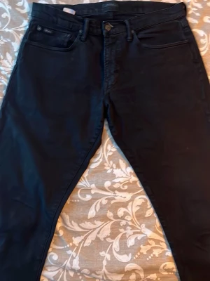 Polo jeans - Säljer ett par svarta slim fit jeans från Polo Ralph Lauren. Storlek W32 L32. Klassisk femficksmodell med knappgylf och diskret logga på myntfickan. Jeansen har en stilren look och är tillverkade i ett mjukt denimtyg med lite stretch för extra komfort. 