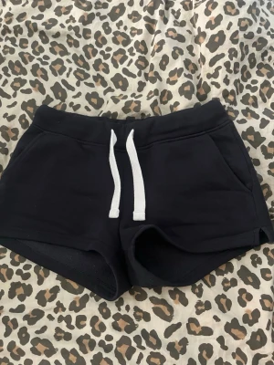 Svarta shorts med snörning - Svarta shorts med vit snörning i midjan och fickor både fram och bak. De har en sportig och avslappnad look, perfekta för sommarens chill dagar. Materialet är mjukt och känns som bomull eller syntet, med en normal passning.