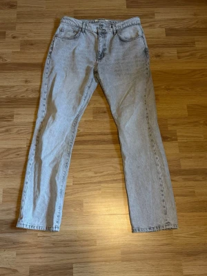 Ljusgrå raka jeans av märket Woodbird  - Säljer ett par ljusgrå jeans med rak passform och klassisk femficksdesign. Jeansen har hög midja och är tillverkade i ett slitstarkt denimtyg. Perfekta för en avslappnad och trendig look. Storlek 32/32