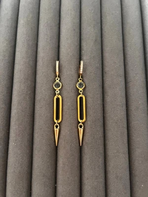 Guldpläterade statement örhängen - Snygga guldpläterade örhängen med svart detalj och spetsig hängande form. Örhängena har en rund svart sten upptill, rektangulär ögla i mitten och en konformad spets längst ner. Perfekta för dig som gillar unika accessoarer med edgy vibe.