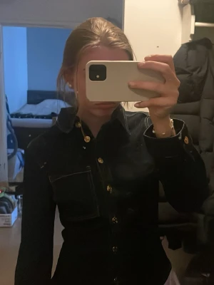 Mörkblå figursydd jeansjacka - Slutsåld mörkblå jeansjacka/tröja med figurnära passform och markerad midja. Jackan har guldiga knappar framtill och på ärmsluten, samt en bröstficka på vänster sida. Klassisk krage och kontrastsömmar ger en stilren look. Perfekt till jeans eller kjol. Kan mötas upp i Stockholm 