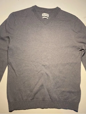 Ljusgrå stickad ull tröja från These Glory Days - Ljusgrå stickad tröja från These Glory Days med V-ringning och ribbade muddar vid ärmslut och nederkant. Tillverkad i mjukt 100% Merino Ull. Passar som en storlek S.