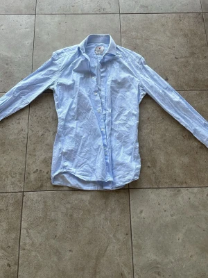 Blåvit rutig skjorta med knappar - Säljer en klassisk blåvit rutig skjorta med lång ärm och knappar framtill. Skjortan har en krage och är tillverkad i ett tunt bomullsmaterial som känns bekvämt och lätt. Perfekt för dig som gillar en stilren look.