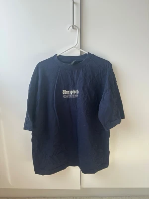 Mörkblå oversized t-shirt  - Säljer en mörkblå oversized t-shirt med tryck både fram och bak i vitt. T-shirten har rund hals och korta ärmar. Perfekt för dig som gillar streetwear och vill ha en avslappnad look.