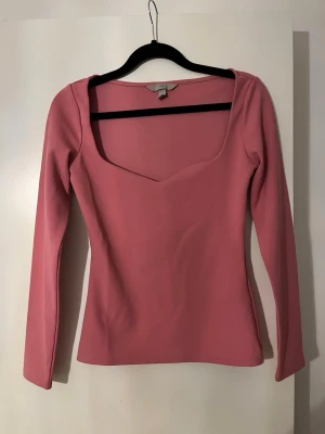 Rosa långärmad topp med fyrkantig ringning - Trendig rosa topp med lång ärm och snygg fyrkantig ringning. Figurnära passform som framhäver siluetten. Perfekt att styla med jeans eller kjol för en cool look.