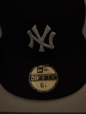 Svart New Era Yankees 59FIFTY keps - Säljer en svart New Era 59FIFTY keps med klassiskt New York Yankees broderat logotyp framtill i vitt. Kepsen har rak skärm och MLB-logga broderad bak. Tillverkad i ett slitstarkt material som ger en clean och sportig look.