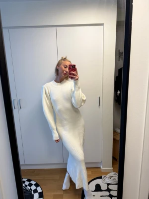 Vit stickad långklänning från Adoore - Vit ribbstickad långklänning från Adoore med rund halsringning och långa ärmar. Klänningen har en figurnära passform och är tillverkad i ett mjukt stickat material som ger en stilren och modern look.