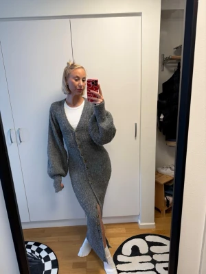 Grå lång stickad kofta från Adoore - Säljer en lång, grå stickad kofta från Adoore med stora ballongärmar och knappar framtill. Koftan har en djup V-ringning och är gjord i ett mjukt, fluffigt material. Perfekt att slänga över en t-shirt för en chill look.