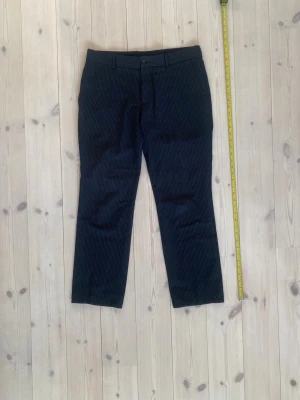Mörkblå randiga kostymbyxor - Snygga mörkblå kostymbyxor med tunna vita kritstrecksränder. Klassisk rak passform med hällor för bälte och sidofickor. Perfekta för en dressad look och passar till skjorta eller kavaj. Materialet känns slätt och stilrent.                                                           Passar dig som är runt 180 med midje mått 30 