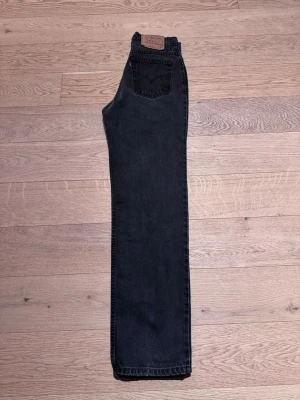 Svarta raka jeans från Levi's - Säljer ett par svarta raka jeans från Levi's med klassisk femficksdesign och läderpatch bak i midjan. Jeansen har hög midja och raka ben, perfekta för en avslappnad och tidlös stil. Materialet är kraftig denim i 100% bomull. Modell 512. Stl Junior M.