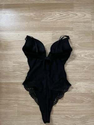 Svart spetsbody med vadderade kupor - Snygg svart body från h&m med vadderade kupor och tunna axelband. Bodyn har spetsdetaljer längs höfterna och benen samt en slät framsida. Original pris 400kr