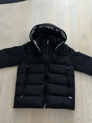 Moncler jacka - Säljer en svart Moncler jacka i fint skick. Klassisk och varm modell med huva och fickor med dragkedja. Storlek M men passar även L. Den yttre dragkedjan är lite trasig men går fortfarande att stänga och använda. I övrigt bra skick.