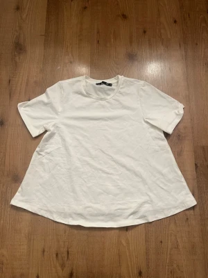 Vit t-shirt med vid passform - Enkel och stilren vit t-shirt med rund hals och korta ärmar. Modellen är lite vidare nertill för en avslappnad look. Perfekt basplagg till garderoben. Väldigt genomskinlig.