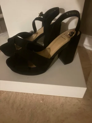 Svarta chunky pumps med öppen tå - Säljer ett par svarta pumps från Vagabond med bred klack och öppen tå. Skorna har en snygg rem över foten och justerbart spänne vid ankeln. Tillverkade i mockaliknande material och har en modern chunky design som ger extra höjd.