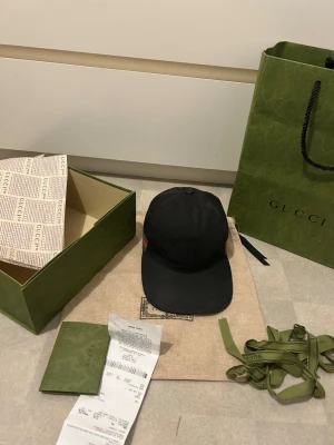 Svart keps från Gucci - Säljer en äkta svart Gucci keps, säljer för jav jag köpt en ny och vill helst få bort den här. Tillbehöret medföljer tyvärr inte  kepsen har små skador men inget som syns när man han på sig den, vänligen fråga om bilder så det inte blir något krångel!