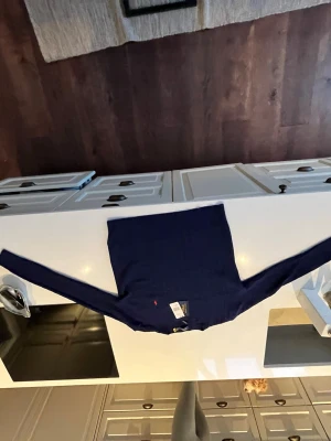 Mörkblå kabelstickad tröja Polo Ralph Lauren - Kabelstickad mörkblå tröja från Polo Ralph Lauren med rund halsringning och lång ärm. Tröjan har en liten röd broderad logotyp på bröstet och är tillverkad i mjukt material. Perfekt för en stilren och klassisk look. Är L men känns som M