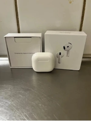 Apple AirPods med laddningsetui - Säljer ett par vita Apple AirPods med trådlöst laddningsetui. Hörlurarna har stilren design, aktiv brusreducering och levereras i originalförpackning. Perfekta för musik, samtal och träning. Materialet är plast och de är smidiga att ta med överallt.