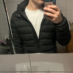 Svart pufferjacka från Colmar - Säljer en svart pufferjacka från Colmar med huva.  Jackan har en stilren design med quiltade paneler och Colmar-logga på ärmen. Perfekt för inför hösten, storlek S passar även M. 