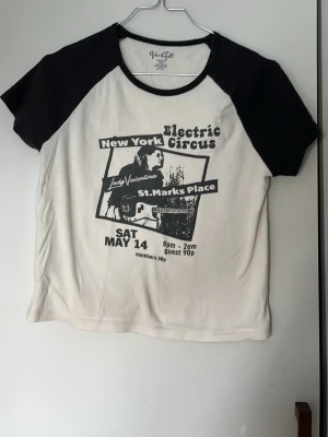 Svartvit t-shirt med tryck från Brandy Melville - Cool svartvit t-shirt från You Girl med kontrastärmar och tryck framtill inspirerat av en konsertposter för Electric Circus i New York. T-shirten har korta ärmar och en croppad passform. Perfekt för dig som gillar retrostil och musikvibe.