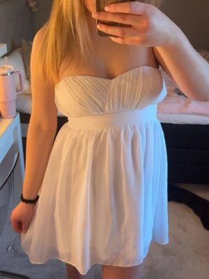 Vit axelbandslös kort klänning - Söt vit axelbandslös klänning med plisserad överdel och markerad midja. Kjolen är lätt utställd och har ett luftigt fall. Perfekt för skolavslutning/student eller annat!