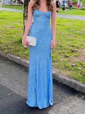 blå klänning med slits - Säljer en lång, glittrig blå klänning med smala axelband och slits på sidan. Klänningen har figurnära passform och är perfekt för balen. Materialet skimrar i ljuset då den har glitterpaljetter. Använd endast 1 gång på min bal men köpt på plick, axelbanden har lite smink på sig men inget man tänker på. Går att knyta så hårt man vill i ryggen, jag är en Xs/S vanligtvis. Jag är 164 och den är lite lång på mig men inget som störde