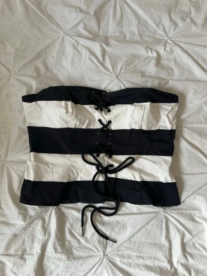 Randig svartvit korsettopp med snörning - Säljer en snygg svartvit korsettopp med breda ränder och snörning framtill. 