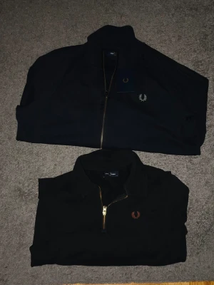 Två tröjor från Fred Perry. Helzipp kostar 599 halvzipp kostar 699, båda för 1250. - Två tröjor från Fred Perry, en med halv dragkedja och en med fullzipp. Fullzippen kostar 1699kr i nypris, den är aldrig använd, taggen sitter kvar och är i helt nytt skick. Halvzippen kostar 2000kr i nypris men kostar mer än den nya då halvzippen är dyrare. Om du bara ska köpa en av dem så får du lämna prisförslag, 599 eller 699 (beroende på vilken du köper). Köper du båda så sparar du 150kr, hör av dig om du har frågor!
