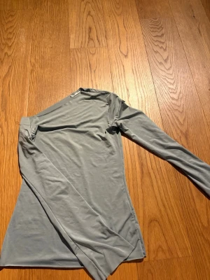 Ljusgrå off shoulder topp - Trendig ljusgrå långärmad topp med off shoulder-design och smal passform. Tillverkad i mjukt, stretchigt material som ger en snygg siluett. Perfekt för dig som vill ha en stilren och modern look.