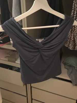 Mörkblå offshoulder topp med twist - Snygg mörkblå offshoulder topp med twistad detalj framtill. Toppen är croppad och har en figurnära passform, perfekt för att lyfta din stil. Tillverkad i mjukt och stretchigt material som sitter skönt på kroppen.💞💞