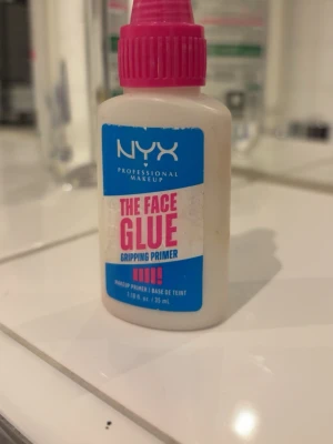 NYX The Face Glue Gripping Primer - NYX The Face Glue Gripping Primer är en primer i en vit plastflaska med blå och rosa etikett samt rosa skruvkork. Produkten är 35 ml och har en smidig applikator. Primern ger ett greppande underlag för makeup och är perfekt för att få sminket att hålla längre. 