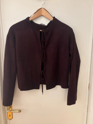 Vinröd kofta med knytning - Säljer en vinröd kofta med långa ärmar och tre knytband framtill. Koftan har en rak, något croppad passform och är tillverkad i ett mjukt tyg. Perfekt att slänga över en topp för en chill look.