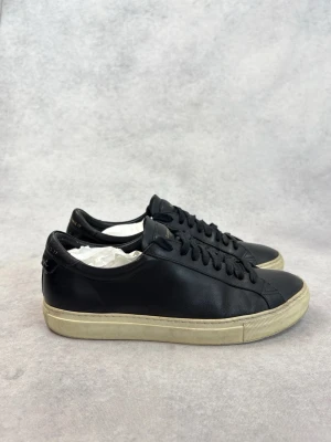 Svarta Givenchy lädersneakers - Svarta sneakers från Givenchy i slätt läder med klassisk låg profil och vit sula. Diskret Givenchy-logga på plösen och hälen. Svarta skosnören och stilren design som passar till det mesta. Perfekta för dig som gillar exklusiva och minimalistiska sneakers.
