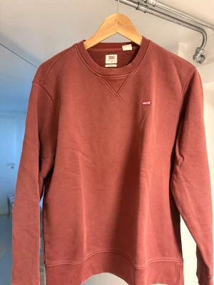 Röd sweatshirt från Levi's - Säljer en stilren röd sweatshirt från Levi's med klassisk rund halsringning och diskret logga på bröstet. Tröjan har långa ärmar och ribbade muddar vid ärmslut och nederkant. Perfekt för en avslappnad look.