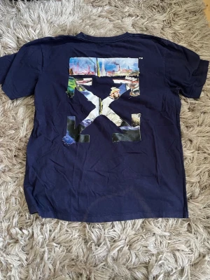 Mörkblå Off-White t-shirt med tryck - Snygg mörkblå t-shirt från Off-White med stort färgglatt grafiskt tryck på ryggen och liten vit logga på bröstet. Klassisk passform och rund halsringning. Perfekt för dig som gillar streetwear och vill sticka ut med en unik design.