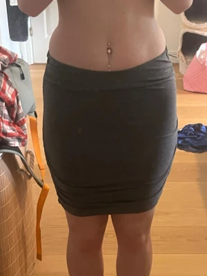 Mörkgrå tight kortkjol - Säljer en enkel och stilren mörkgrå tight kjol i kort modell. Kjolen har en rak passform och är gjord i ett mjukt stretchigt material som sitter skönt på kroppen. Perfekt att matcha med en crop top eller hoodie för en avslappnad look. Använd mycket men inga tecken på slitage. 